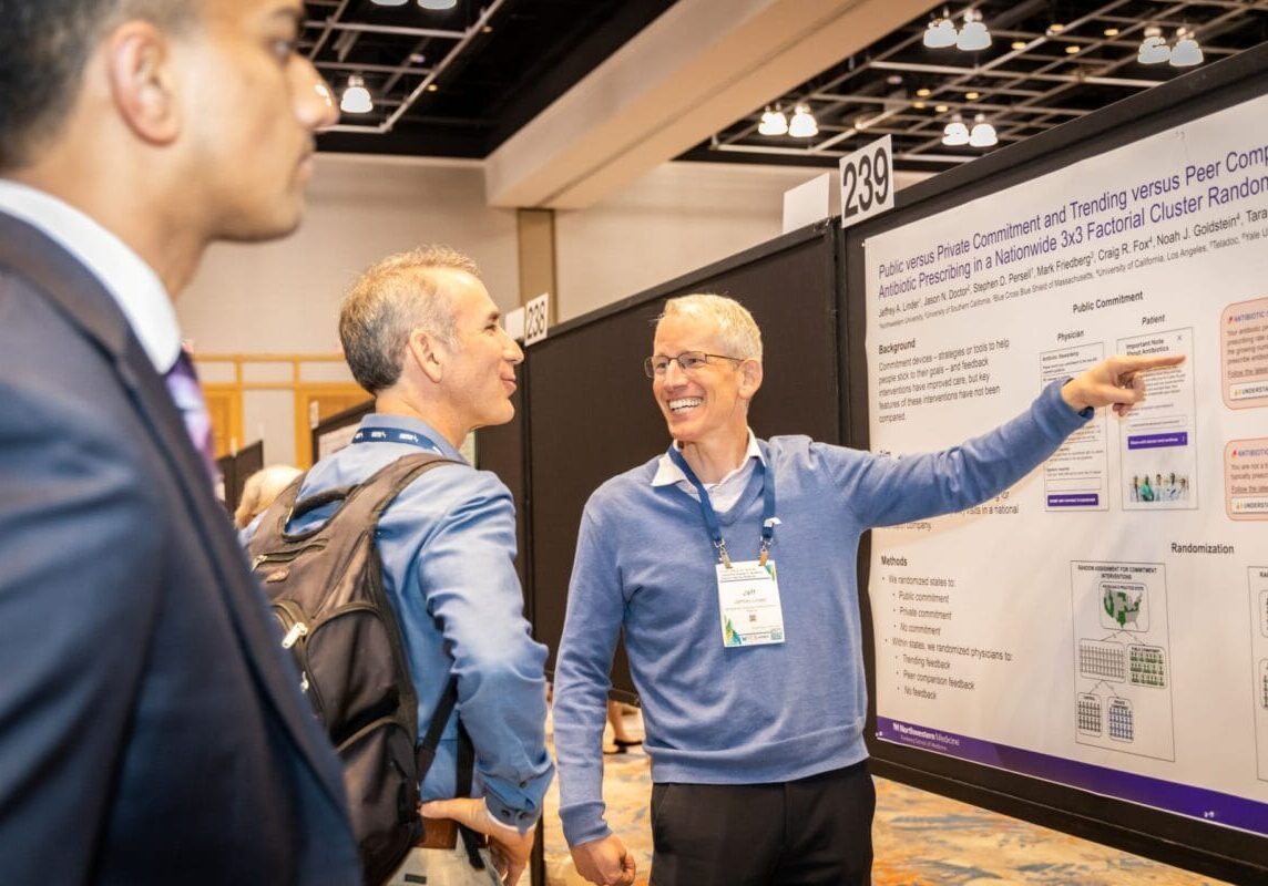 Conference attendee points to poster and addresses other attendees
