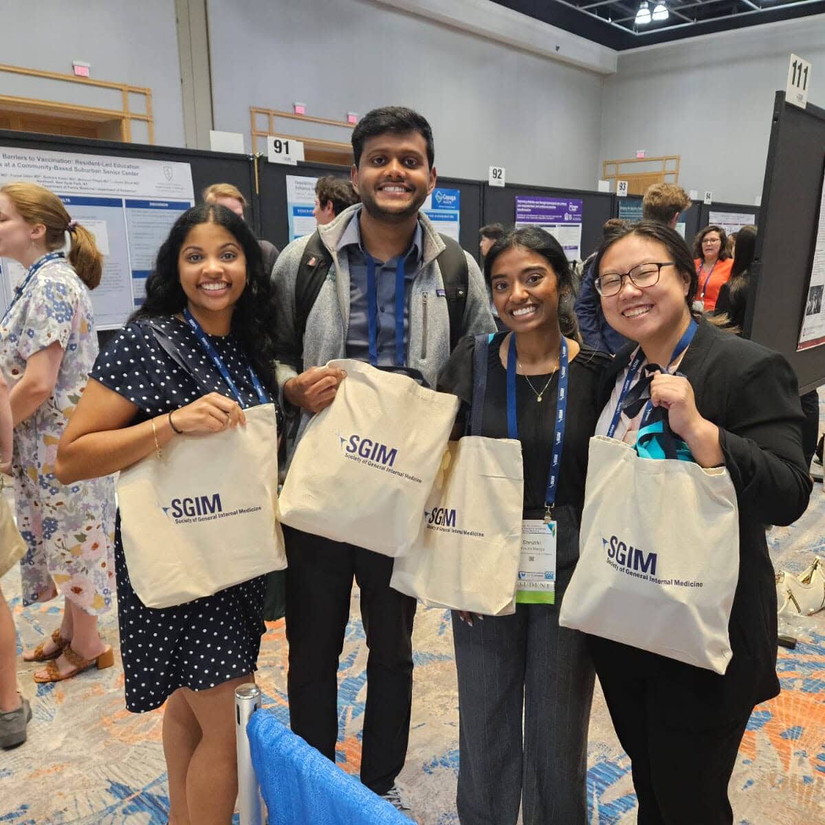 Four conference attendees holding SGIM bags posing for a photo